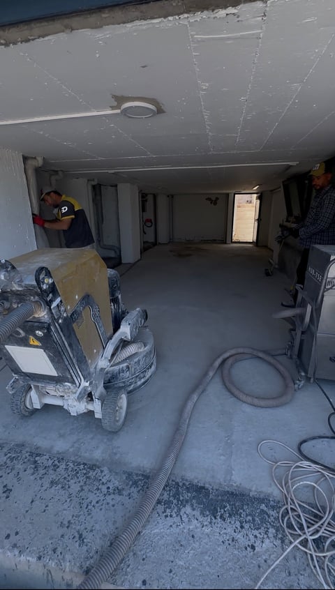 Interior of garage under renovation with exposed ceiling, construction equipment, and workers in background