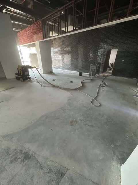 Industrial warehouse interior under construction with concrete floor, exposed brick walls, steel framework, and construction equipment